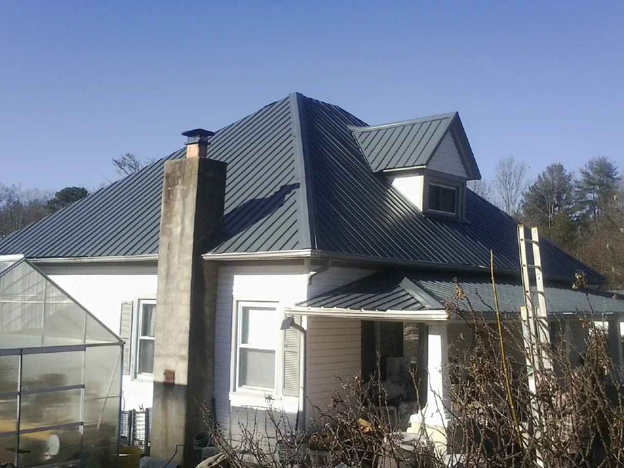 Dark blue standing seam metal roof on a white farmhouse with dormer — Slate & Tile Roof Repair by Roofing Brothers in Lake Arrowhead