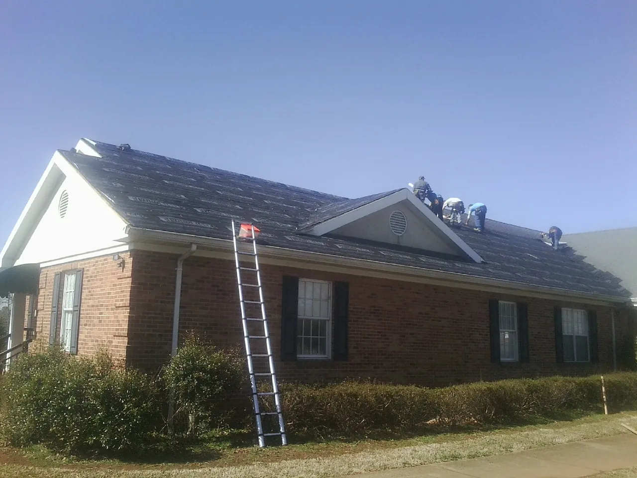 Crew tearing shingles off a brick ranch roof with a ladder set — Emergency Roof Repair work by our crew in Lake Arrowhead