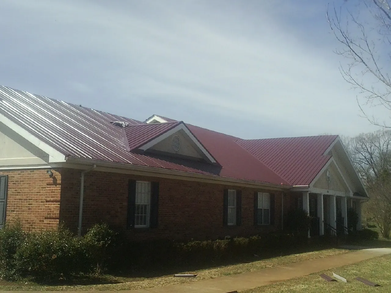 Red metal roof with gabled entries on a long brick building, from a Hail Damage Roof Repair job in Lake Arrowhead
