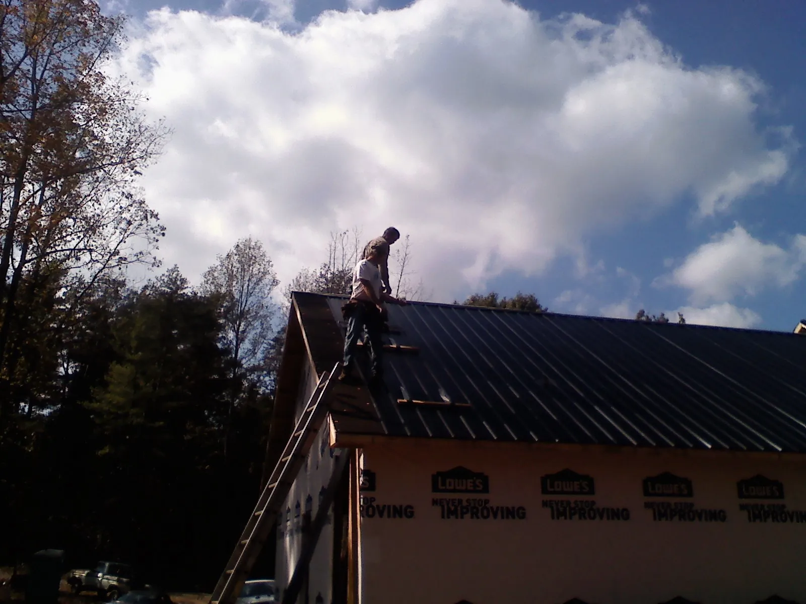 Roofer fastening dark metal panels high against a cloudy sky, from a Roof Inspection job in Lake Arrowhead