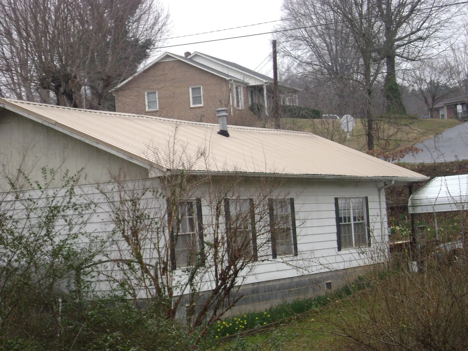Tan metal roof on a white sided house set into a hillside — Commercial Roofing by Roofing Brothers in Lake Arrowhead